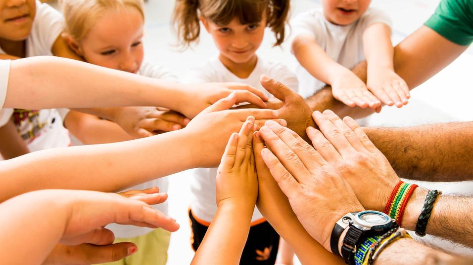 Kinder und Erwachsene legen ihre Hände in einem Kreis zusammen, symbolisieren Zusammenarbeit und Gemeinschaft.