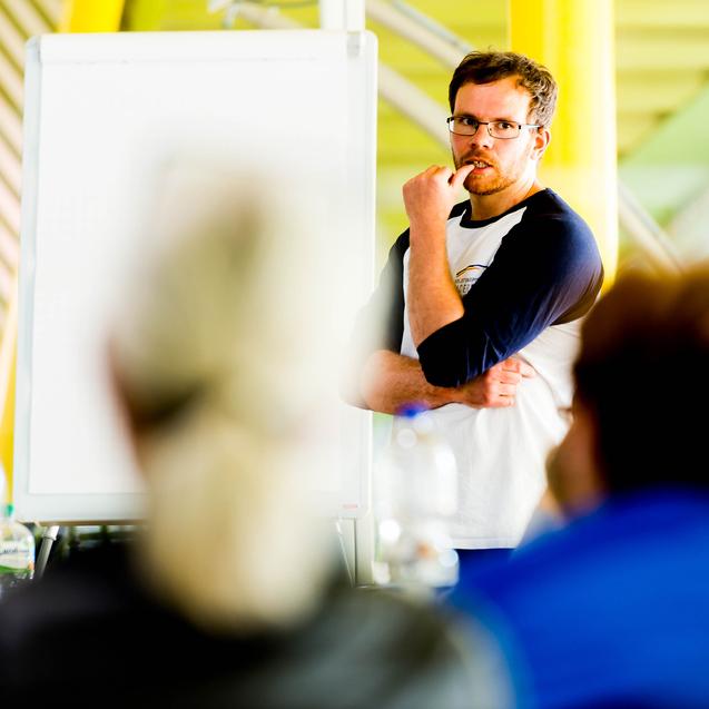 Mann mit Brille spricht vor einer Gruppe, ein Flipchart ist im Hintergrund sichtbar.